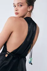 Vestido midi negro de tejido sastrero fino y liso con leve brillo. Tiene escote en V, tiras para ajustar en la cintura, volado asimétrico en el ruedo y espalda descubierta.