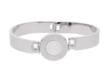 Pulsera rígida plateada de acero inoxidable con diseño de números romanos alrededor de un círculo central reversible con una cara de nácar y otra de ónix.