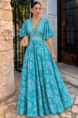 Vestido largo turquesa con estampado floreado y detalles geométricos, escote en V profundo, mangas cortas con volados y diseño fluido.