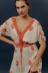 Vestido largo beige con estampado paisley en color azul marino, escote en V profundo con detalle bordado, mangas cortas amplias, cordón ajustable en la cintura con borlas y volados en el ruedo.