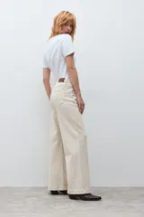 Jean de corte wide leg en color beige claro, con tiro medio y cierre frontal con botón y cremallera. Presenta un diseño de cinco bolsillos y costuras reforzadas.