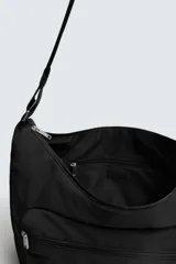 Bolso de hombro tipo hobo o media luna, confeccionado en tejido técnico negro. Presenta un bolsillo frontal con cierre y una correa ajustable para llevar al hombro.
