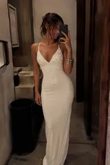 Vestido largo color marfil de corte sirena, con escote en V pronunciado, tirantes finos y aplicaciones de pedrería y tachas metálicas distribuidas en el frente.