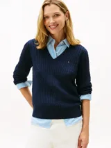 Sweater Tommy Hilfiger de punto trenzado color azul marino, de manga larga con cuello en V y detalles acanalados en puños y dobladillo. Presenta el logo de la marca bordado en el pecho.