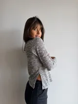 Remera básica de manga larga y cuello redondo, confeccionada en tejido melange en tonos grises y blancos con sutiles destellos multicolores. Presenta un corte recto con aberturas laterales en el dobladillo.