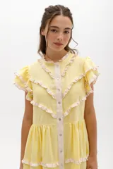 Vestido midi de lino blanco con diseño de broderie, cuello alto, cierre frontal con botones y volados decorativos en los hombros y el cuerpo.