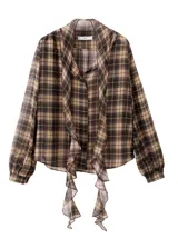 Blusa de poliéster con estampado a cuadros en tonos marrones y negros, con cuello camisero, manga larga y detalle de volados en la parte delantera.