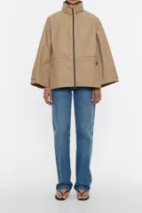 Chaqueta tipo gabardina corta de tejido técnico con corte en línea A, cuello alto con capucha plegable, cierre frontal con cremallera y mangas anchas con trabillas en los puños.