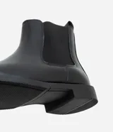 Bota tipo Chelsea de caña media, color negro, con paneles laterales elásticos y suela de goma. Diseño de punta redonda y estilo minimalista.