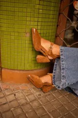 Sandalia de gamuza color marrón, con taco ancho, punta fina y tira ajustable al tobillo. Incluye detalle metálico en la puntera.