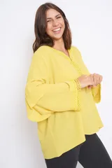 Blusón amarillo con escote en V y detalle de galón en cuello y mangas. Mangas anchas con volados y corte oversize.