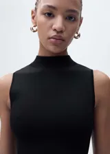 Vestido largo de punto con cuello perkins y diseño sin mangas. Presenta un corte ajustado en el torso que se abre en una falda evasé con textura acanalada en la parte inferior.