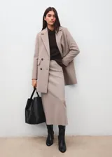 Abrigo de paño color beige, con diseño cruzado de doble botonadura, solapas clásicas y bolsillos laterales con solapa. Presenta un corte estructurado y elegante.