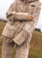 Sweater oversize de lana natural con estampado cuadrillé en tonos azul, verde y rojo. Presenta cuello alto, mangas largas y detalles de flecos torneados en el cuello, puños y dobladillo.