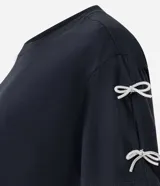 Camiseta blanca de algodón con cuello redondo y mangas cortas, decorada con pequeños lazos brillantes en los laterales de las mangas.