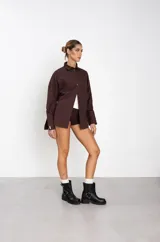 Botas de caña baja en cuero sintético color marrón, con diseño de estilo biker que incluye dos correas horizontales con hebillas metálicas y una argolla decorativa en el lateral. Posee suela y taco bajo de color negro.