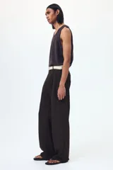 Pantalón sastrero de sarga en color marrón oscuro, con corte holgado, piernas amplias con raya marcada, cierre frontal con botón y corchete ocultos, bolsillos laterales al bies y bolsillos traseros insertados.