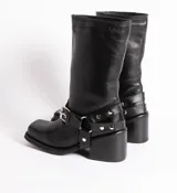 Bota de cuero negra con caña media, punta cuadrada, taco bloque y arnés con hebillas y tachas plateadas.