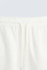 Bermuda de algodón color beige claro, de corte regular fit, con cintura elástica ajustable mediante cordón. Presenta bolsillos laterales y un bolsillo trasero de vivo.