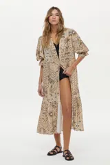 Vestido túnica de lino y viscosa, color camel con estampa artesanal en tonos oscuros, escote en V profundo, mangas amplias abullonadas y falda larga con volado en el ruedo.