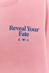 Camiseta oversize de manga corta y cuello redondo, color rosado con efecto lavado, con pequeño texto estampado en azul en el pecho.