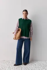 Chaleco tejido de punto color beige, con cuello redondo, terminaciones en rib y lazos laterales regulables que permiten ajustar la prenda.