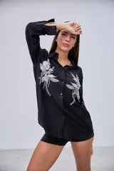 Camisa negra de manga larga con cuello clásico y botones frontales. Presenta dos grandes apliques bordados con lentejuelas y cuentas en forma de flores y hojas en la parte delantera.