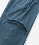 Pantalón de corte holgado en color azul petróleo, confeccionado en microfibra de poliéster. Presenta un diseño utilitario con múltiples bolsillos funcionales, cierres visibles y detalles técnicos en las piernas.