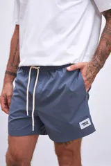 Short de baño color celeste, con cordón ajustable en la cintura y un parche cuadrado negro con el logo "HAUS" en blanco en la pierna izquierda.