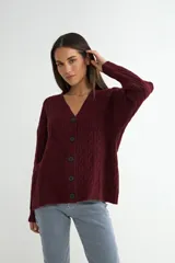 Cardigan de punto con diseño de trenzas, color beige, con escote en V, cierre frontal de botones negros y mangas largas con puños acanalados.
