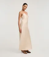 Vestido largo (midi) color beige claro, estilo slip dress, con escote en V y breteles finos ajustables. Presenta un recorte sutil en el área del busto.