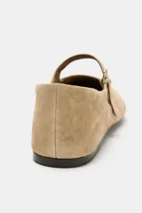 Zapato tipo bailarina de ante color beige, con punta redonda, suela plana de 1 cm y tira delantera con hebilla metálica.