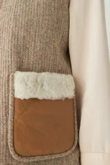 Chaleco corto de corte recto, confeccionado en lana fina sin teñir, con cuello de piel sintética y bolsillos frontales con detalles en cuero.