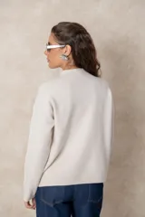 Buzo de punto color visón con cuello alto, manga larga y diseño holgado. Presenta un bordado floral en relieve al tono en la parte frontal.