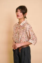 Camisa de manga larga color beige con delicado estampado floral multicolor, cuello camisero y cierre frontal de botones.