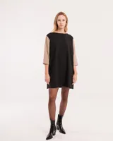 Vestido corto negro con mangas 3/4 verdes, cuello bote y bolsillos laterales.