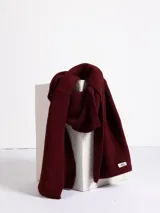Bufanda de tejido de punto acanalado en color bordó, con etiqueta de marca Haus en uno de sus extremos.