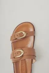 Sandalias planas de cuero negro con diseño de dos tiras ajustables con hebillas metálicas.