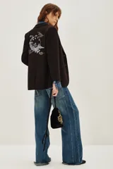 Saco sastre de color negro con corte clásico y solapas. Presenta un bordado artístico en la espalda con motivos de montañas, nubes y flores en tonos suaves.