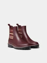 Botas de agua de caña baja color bordó, con elásticos laterales a rayas en tonos burdeos, beige y marrón. Cuenta con suela dentada negra, costuras blancas decorativas en el borde y presilla trasera para facilitar el calce.