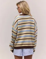 Cardigan tejido de punto con diseño a rayas horizontales en tonos crema, celeste y marrón. Presenta cuello redondo, cierre frontal con botones y mangas largas con puños acanalados en color marrón.