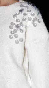 Buzo color crema de punto con escote redondo y lentejuelas bordadas en los hombros.