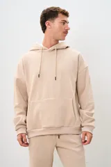Buzo canguro beige de corte holgado con capucha y cordones ajustables.