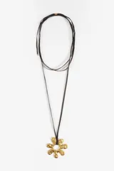 Collar largo con cordón de gamuza sintética en color negro y dije central de metal dorado con forma de flor orgánica de diseño irregular.