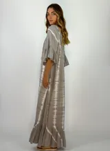 Vestido largo de corte holgado con estampado tie-dye en tonos grisáceos. Presenta escote redondo con cordones ajustables y borlas, mangas tres cuartos con volados y ruedo con volado amplio.