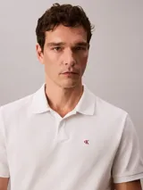 Chomba blanca de piqué de algodón, corte clásico, cuello tradicional, cartera de botones y bajo con aberturas laterales. Tiene un logo bordado en el pecho.