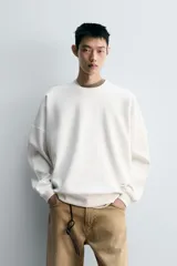 Sudadera negra de corte relaxed fit, confeccionada en tejido técnico interlock de algodón con elasticidad. Presenta cuello redondo, manga larga y una etiqueta aplicada en el bajo. Los acabados son en rib.