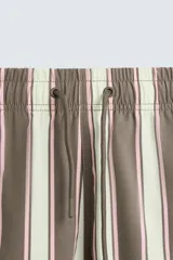 Bañador de hombre con estampado de rayas verticales anchas en tonos marrón oscuro y beige claro, con finas líneas rosadas entre ellas. Posee cintura elástica con cordón ajustable y forro interior.