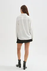 Camisa de viscosa blanca de corte holgado, con mangas largas, cuello camisero, cierre frontal con botones y detalle de bolsillo otonado en el pecho.