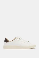 Zapatilla deportiva tipo bamba color blanco, con detalle de talonera en contraste color marrón oscuro y suela de plataforma engomada en tono crema.
